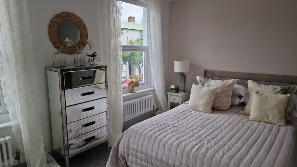 Living Room & Bedroom Renovation | London & Home Counties 5 A bedroom featuring a bed with cushions, a dresser, and a lamp beside a window. - London