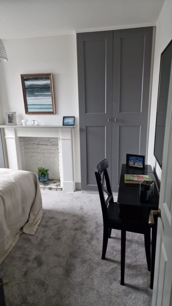 Living Room & Bedroom Renovation | London & Home Counties 10 A bedroom featuring a grey wardrobe, a small black desk, and a bed with a light-coloured blanket. - London