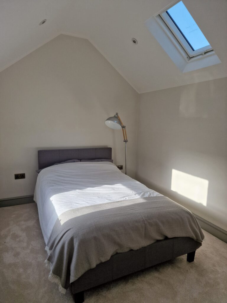 Living Room & Bedroom Renovation | London & Home Counties 14 A minimalist bedroom featuring a double bed with a grey blanket and a skylight above. - London