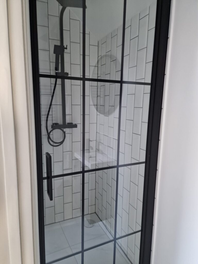 Shower cubicle featuring black framed glass and white tiled walls with a round mirror. - London