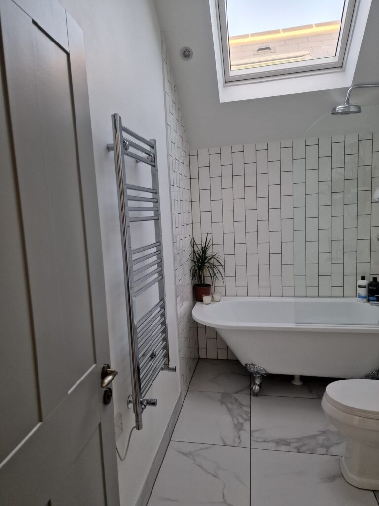 Interior view of a modern bathroom featuring a bathtub, heated towel rail, and tiled walls. - London
