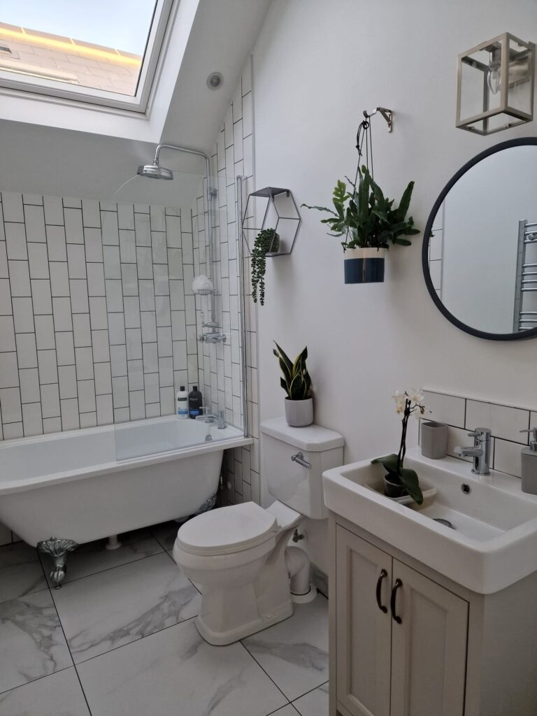A modern bathroom featuring a freestanding bathtub, plants, and a round mirror. - London