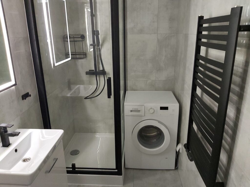 Contemporary bathroom featuring a shower enclosure, washing machine, and heated towel rail. - London