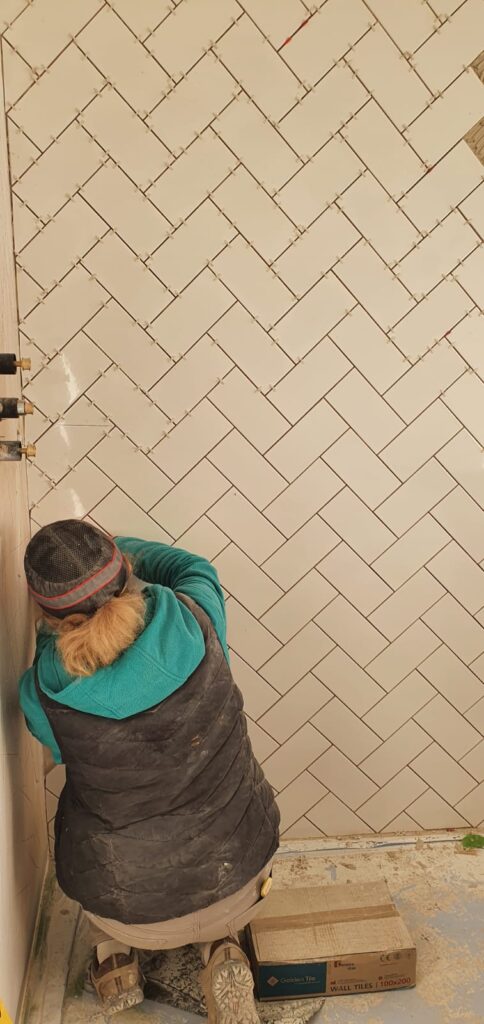 Person installing white tiles in a herringbone pattern on a wall. - London