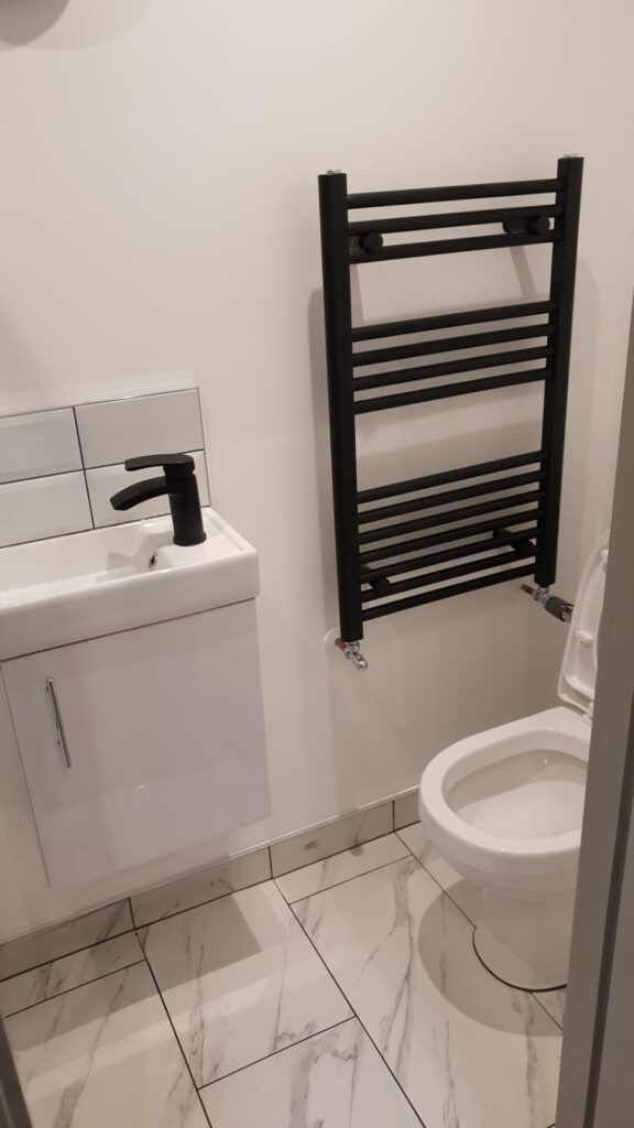 Compact bathroom featuring a wall-mounted towel radiator and a white toilet with a small sink. - London
