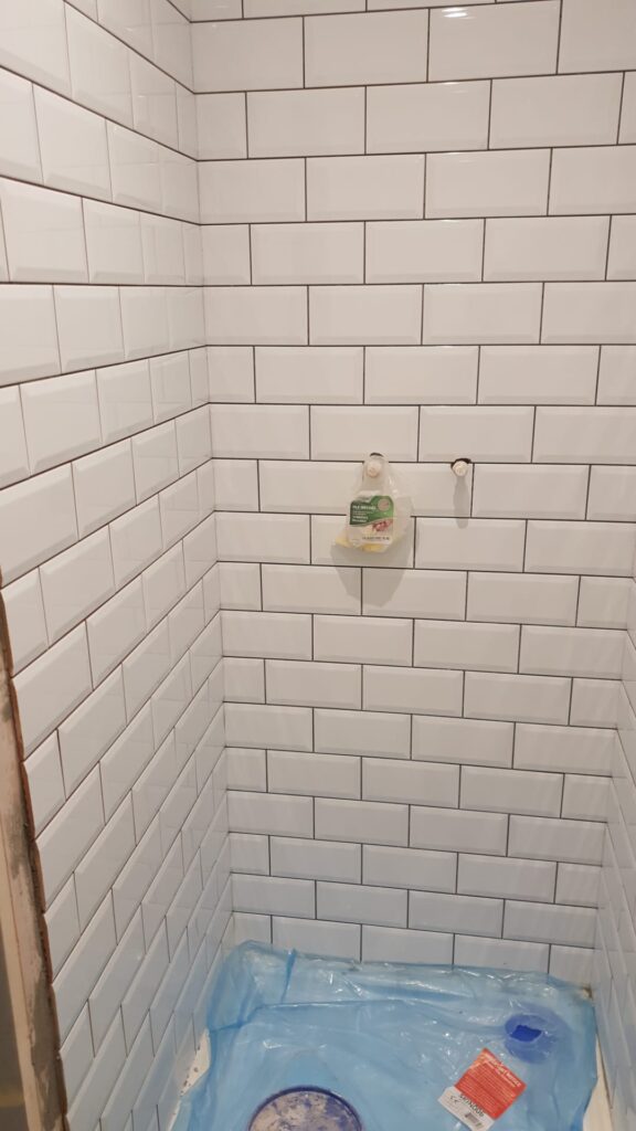 Shower wall featuring white subway tiles arranged in a grid pattern. - London
