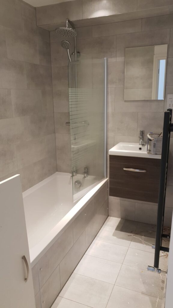 A modern bathroom featuring a bathtub with a glass screen and a wall-mounted sink with a cabinet. - London