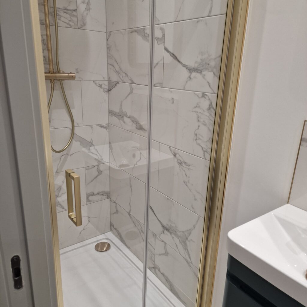 A modern shower enclosure featuring marble tiles and a gold shower fixture. - London