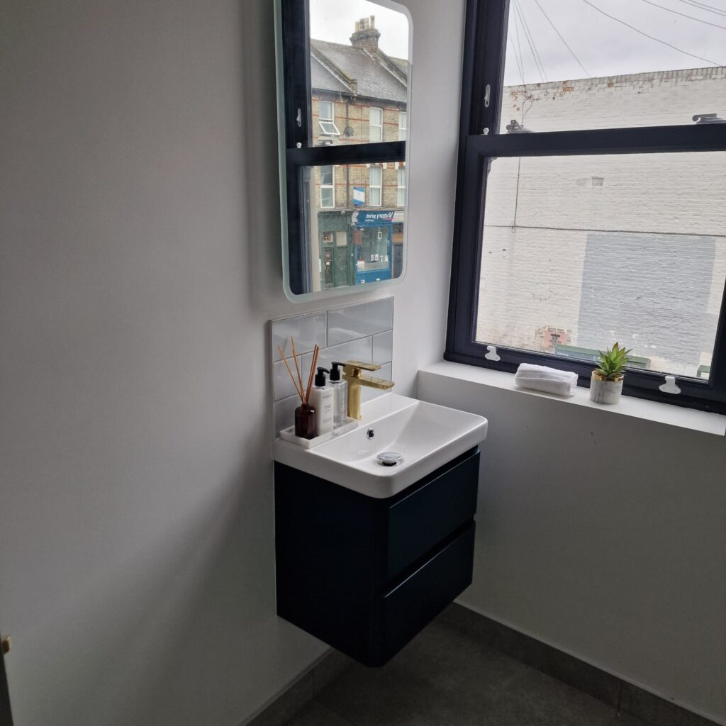 Compact bathroom sink with a mirror above and toiletries on the countertop. - London