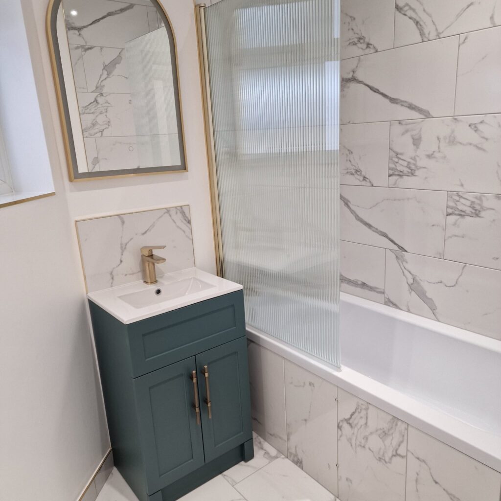 Bathroom featuring marble wall tiles, a green vanity unit, and a shower screen. - London