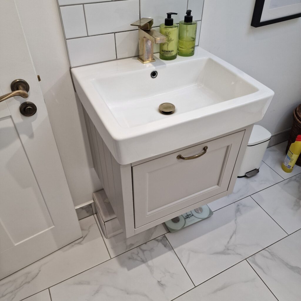 White ceramic bathroom sink with a cabinet below and toiletries on the countertop. - London