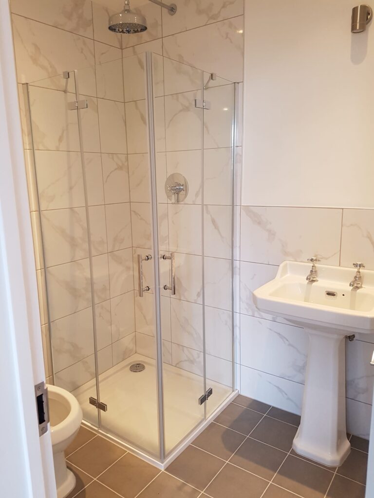 Glass shower enclosure with a rainfall showerhead and a pedestal sink in a bathroom. - London