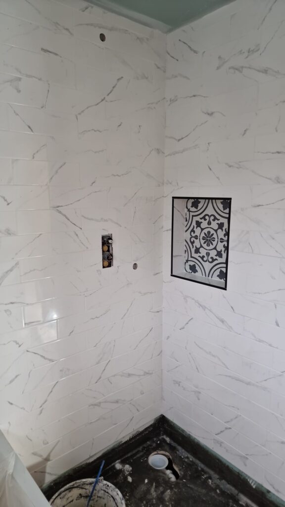 Bathroom wall featuring white marble effect tiles and a decorative tile insert. - London