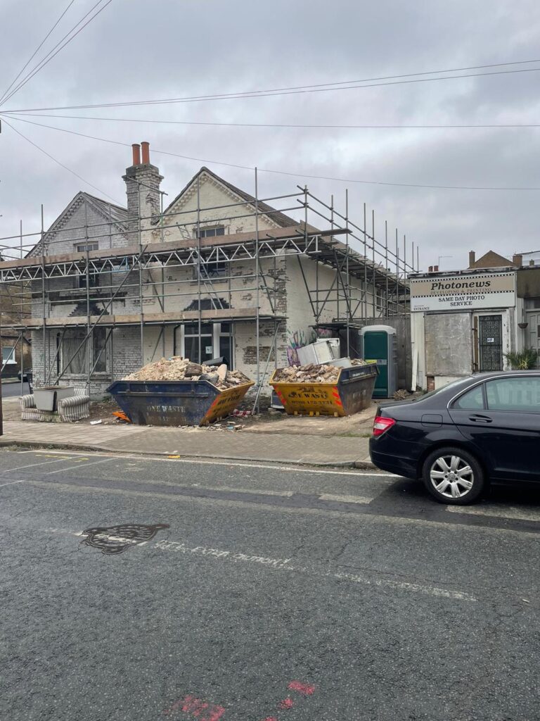 Garden Buildings & Outdoor Spaces | London & Home Counties 18 Two waste bins filled with construction debris outside a building under renovation with scaffolding. - London