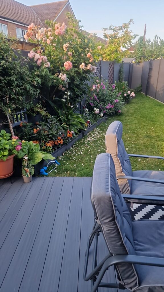 Garden Buildings & Outdoor Spaces | London & Home Counties 26 A garden featuring various flowering plants and a grey seating area on a wooden deck. - London