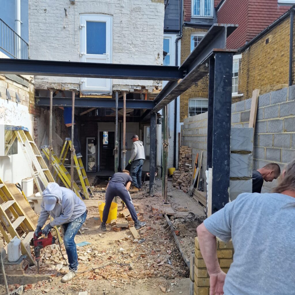 Garden Buildings & Outdoor Spaces | London & Home Counties 27 Workers engaged in construction activities at a building site with tools and materials visible. - London