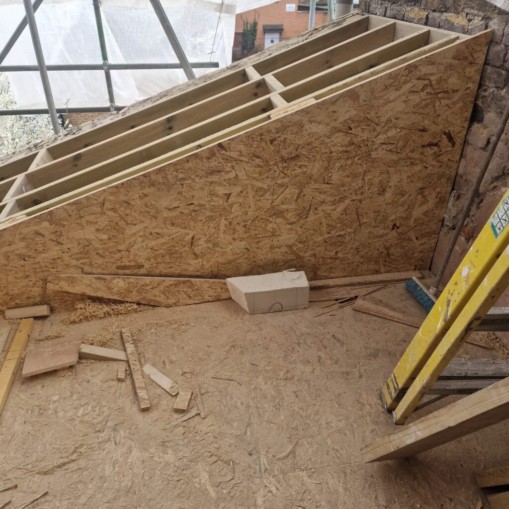 Plywood sheets and wooden beams arranged on a construction site floor with tools nearby.