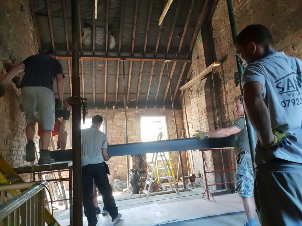 Construction workers lifting a beam during a renovation project in a brick building. High Wycombe