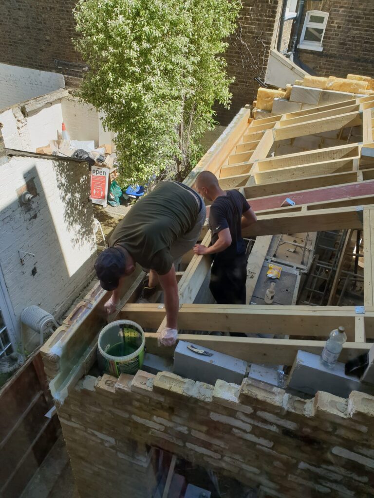 Two construction workers installing wooden beams on a building roof during renovation. Slough
