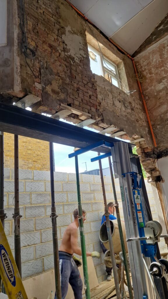 House Extensions | London & Home Counties | 30+ Years Experience 2 Exposed brick wall during interior construction with scaffolding and workers present.