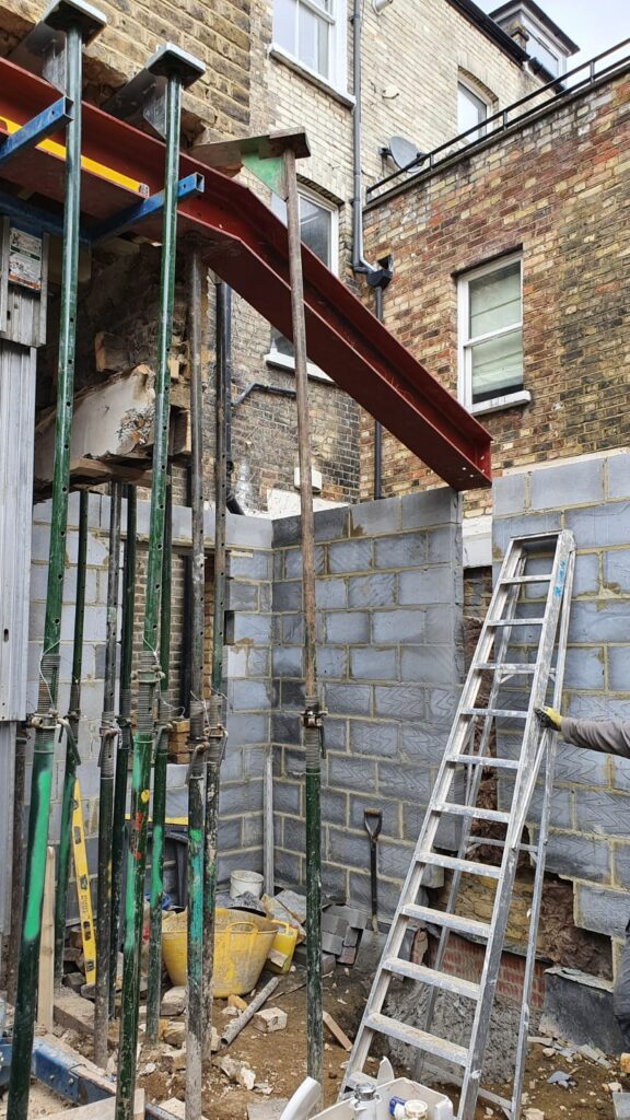 House Extensions | London & Home Counties | 30+ Years Experience 3 Construction site featuring steel beams, scaffolding, and a ladder against a brick wall.