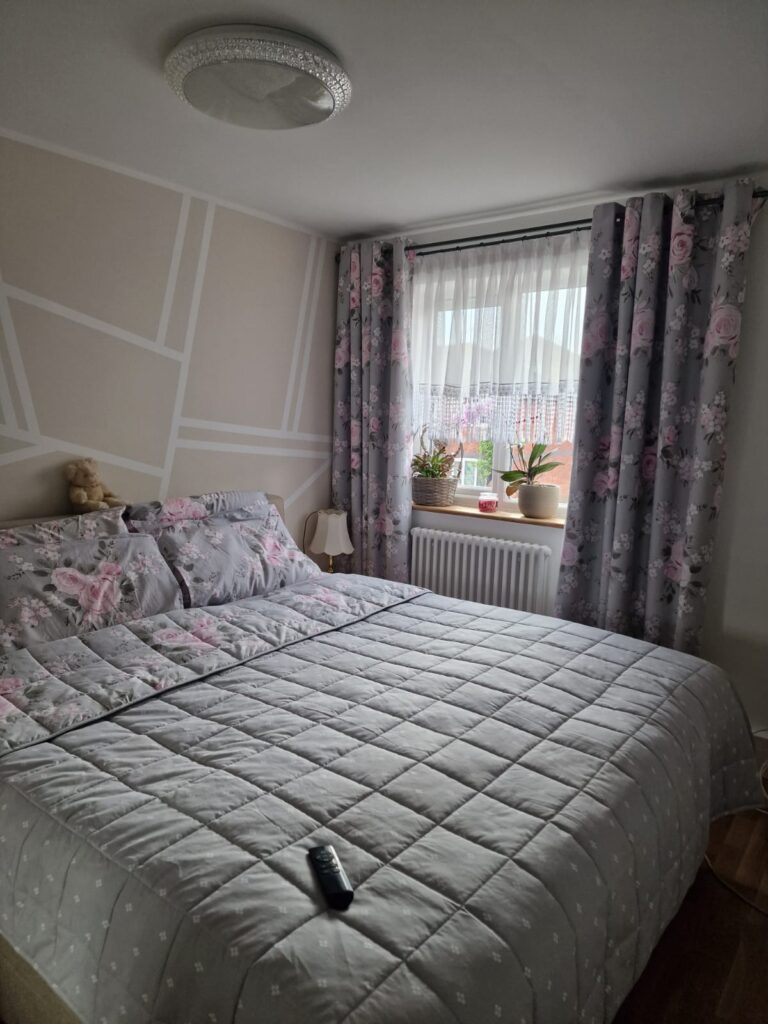 Living Room & Bedroom Renovation | London & Home Counties 27 A grey bed with floral bedding and a remote control on top in a bedroom setting. - London