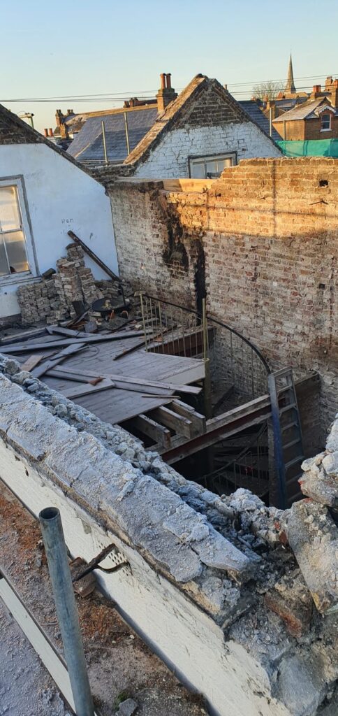Interior view of a collapsed building showing exposed walls and debris on the floor.