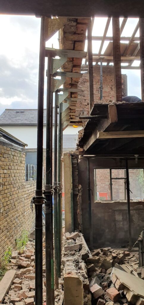 House Extensions | London & Home Counties | 30+ Years Experience 6 View of a construction site showing exposed brick walls and scaffolding supports.