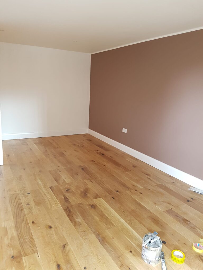 Living Room & Bedroom Renovation | London & Home Counties 25 Interior view of a room with a brown feature wall and wooden flooring, with paint cans on the floor. - London