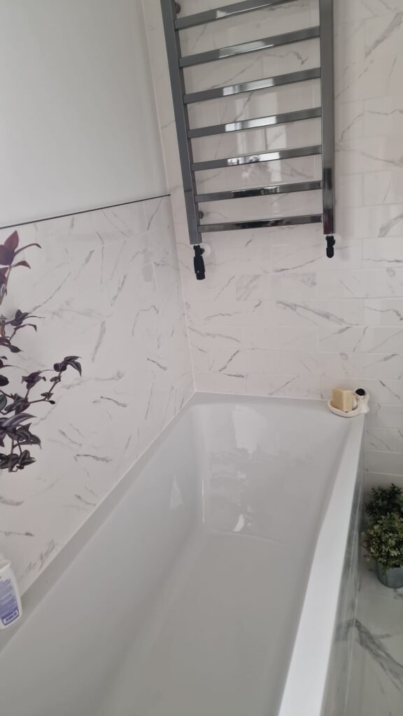 A modern white bathtub set against a marble wall with a towel rail above. - London