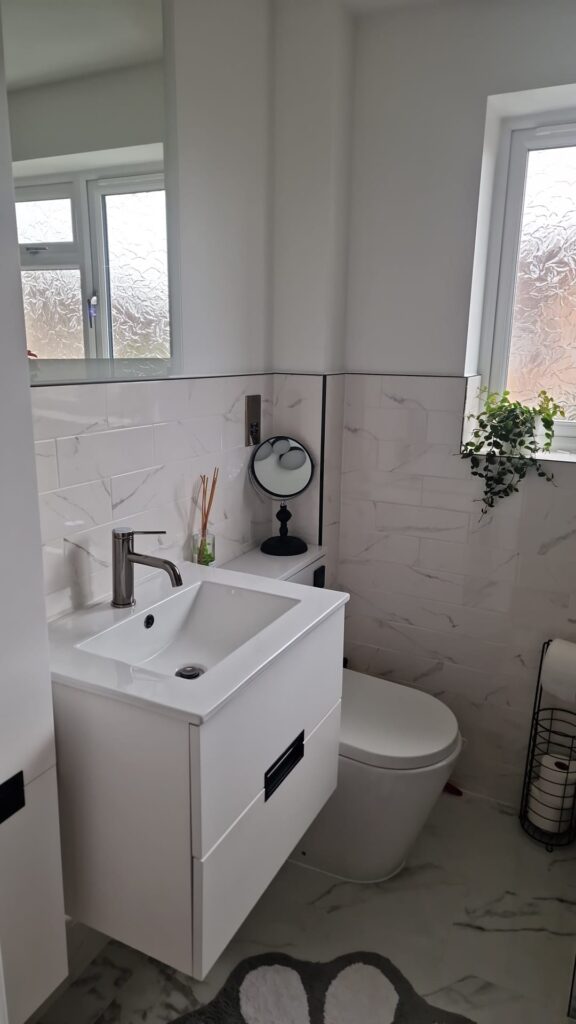 Contemporary bathroom featuring a white sink, toilet, and mirror with natural light from a window. - London