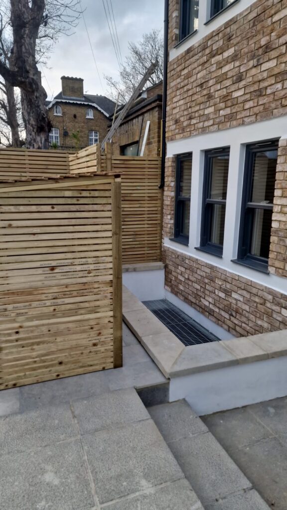 Garden Buildings & Outdoor Spaces | London & Home Counties 34 Wooden fencing panels surrounding a stone step area with a drainage grate.